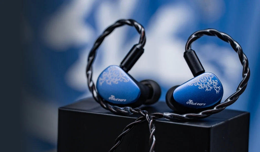 Blue and black in-ear earphones with decorative white floral patterns on the ear tips, resting on a black display block against a blurred blue background.