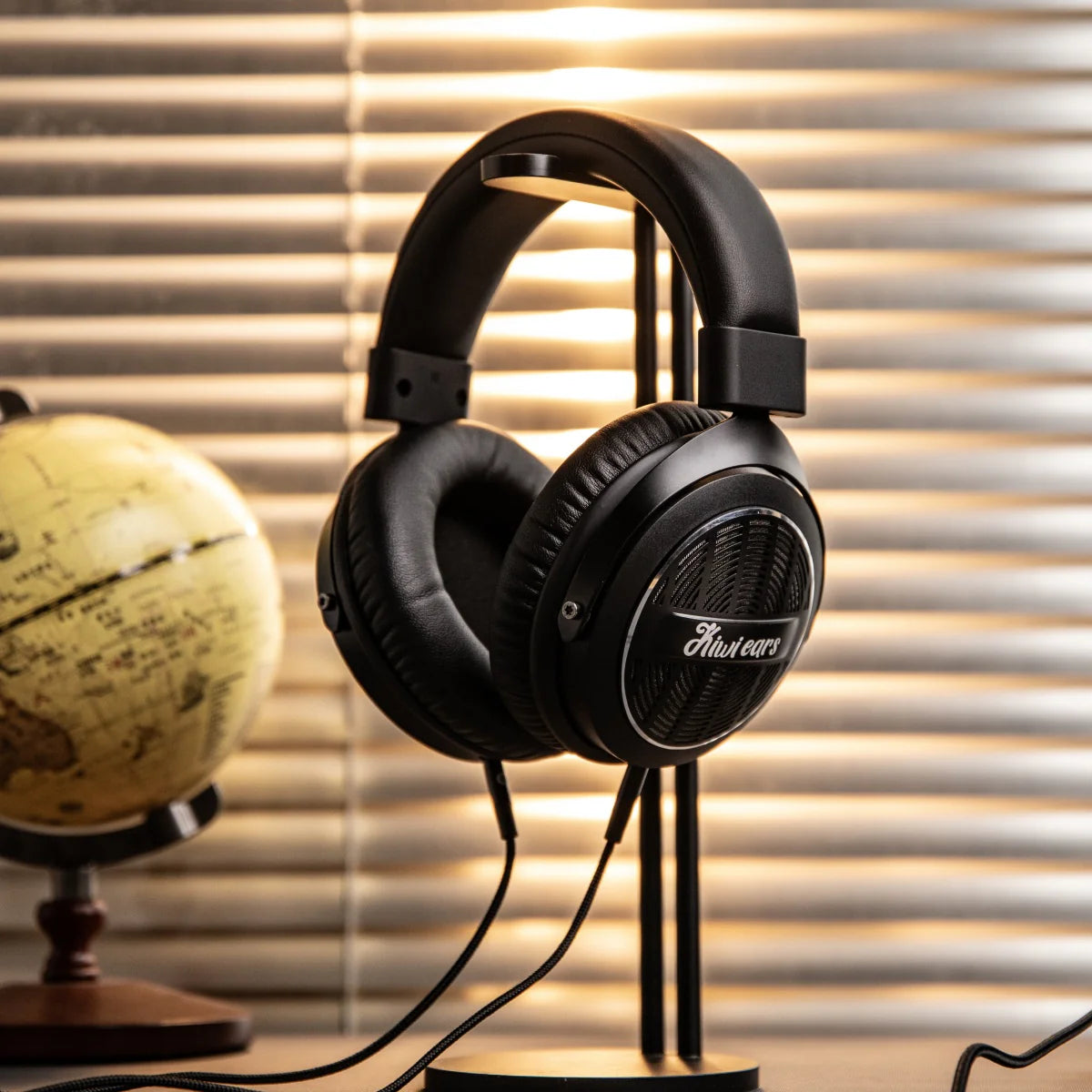 Kiwi Ears Ellipse headphones, set against a background of warm window blinds with a vintage globe on the left.