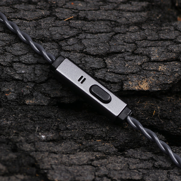 A close-up of a gray wired earbud controller with a switch and three small indicator slots, resting on dark textured bark.