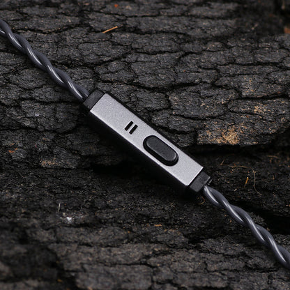 A close-up of a gray wired earbud controller with a switch and three small indicator slots, resting on dark textured bark.
