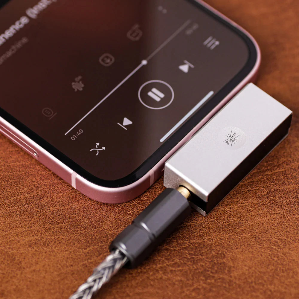 A close-up of allergo mini DAC connected to a smartphone, resting on a brown textured leather surface.