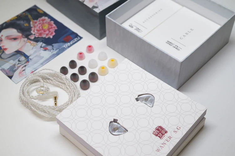 A pair of in-ear monitors with a white braided cable, shown alongside multiple ear tips, an open presentation box, and a branded package on a clean white surface.