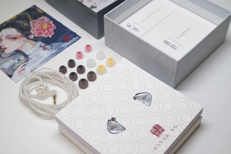 A pair of in-ear monitors with a white braided cable, shown alongside multiple ear tips, an open presentation box, and a branded package on a clean white surface.