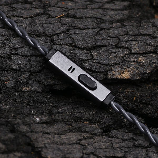 A close-up of a gray wired earbud controller with a switch and three small indicator slots, resting on dark textured bark.