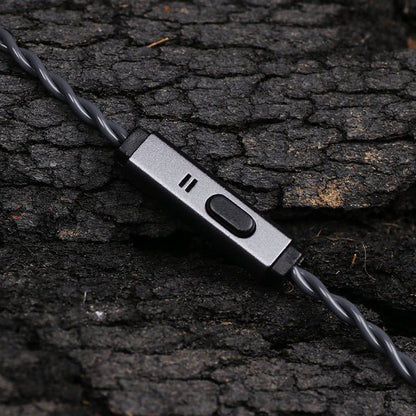 A close-up of a gray wired earbud controller with a switch and three small indicator slots, resting on dark textured bark.